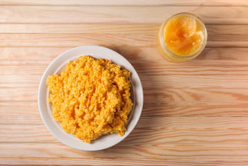millet boiled porridge with pumpkin in a plate on a wooden background. in the jar honey is open