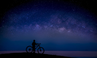 Fototapeta na wymiar Boy and bike on the mound and the Milky Way in the sky; Long exposure photograph, with grain.Image contain certain grain or noise and soft focus. 