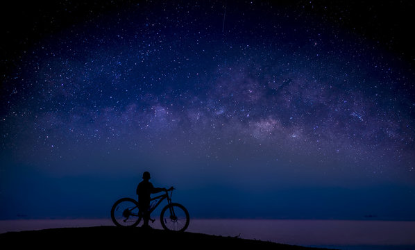 Boy and bike on the mound and the Milky Way in the sky; Long exposure photograph, with grain.Image contain certain grain or noise and soft focus.
