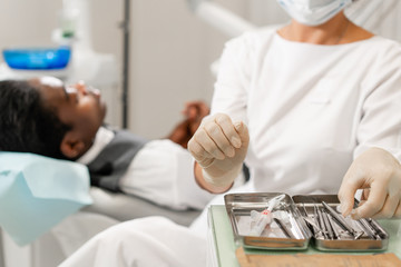 Dental instruments in the foreground. Woman dentist treating root canals in the dental clinic. Man patient lying on dentist chair with open mouth. Medicine, dentistry and health care concept.