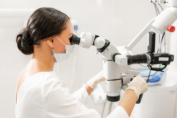 Female dentist advanced user, dental tools. Looking into the lens of a microscope while examining...