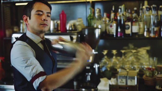 Asian bartender shaking cocktail with ice inside shaker on bar counter backround. Slow motion