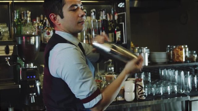 Asian bartender shaking cocktail with ice inside shaker on bar counter backround