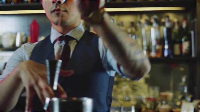 Asian bartender spills beverage into jagger. Film look and big bar counter