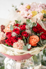 two beautiful fresh cut bouquet of mixed flowers in vase on wooden table. The work of the florist at a flower shop. Red spray roses and other flowers