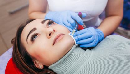 Doctor injecting in a beautiful face of a young woman. Plastic surgery concept.