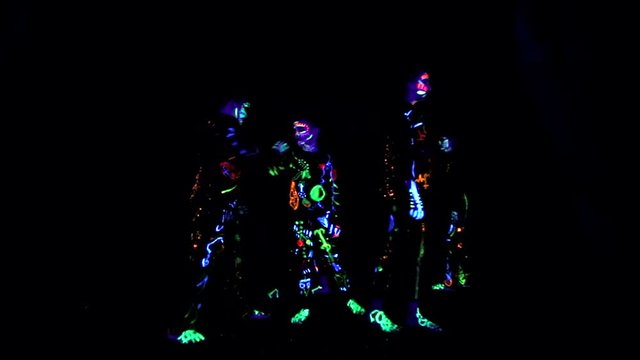 creative group of children in colorful costumes that glow in the dark, creates abstract movements. The costumes that glow in the dark room are painted in paints