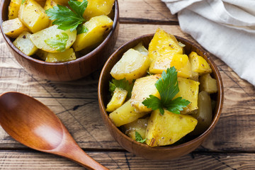 Baked potatoes with spices and herbs in wooden plate.