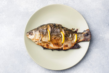 Baked fish carp with lemon greens on a plate.