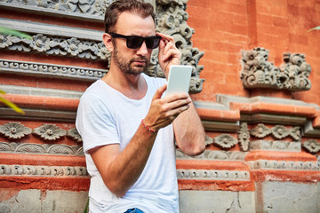 Man with sunglasses and summer shirt using smartphone.