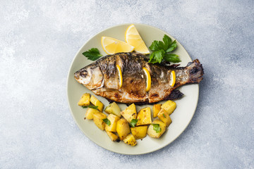 Baked fish carp with lemon greens and potatoes on a plate. Copy space