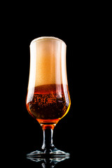 A glass of beer with foam hat on black background