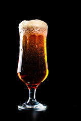 A glass of beer with foam hat on black background
