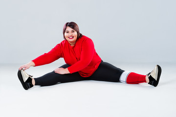 Plus size model in sportswear, fat woman doing workout on gray background, healthy lifestyle concept