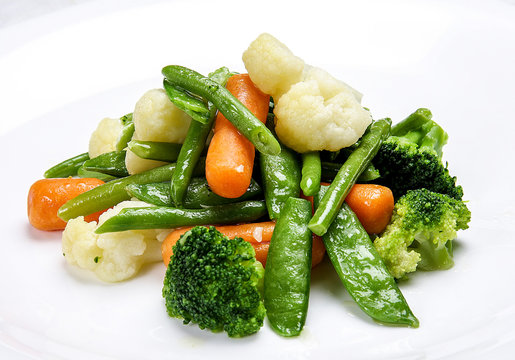 Steamed vegetables on white background. Cauliflower, peas, broccoli, carrots and asparagus beans.