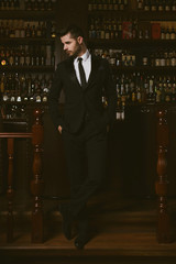 Attractive man wearing black tuxedo in whiskey bar.