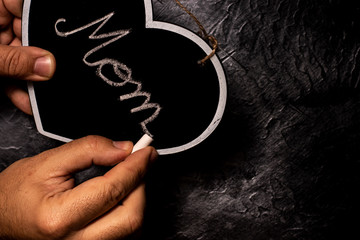 Writing mom word on heart shape slate board