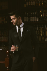 Attractive man wearing black tuxedo in whiskey bar.