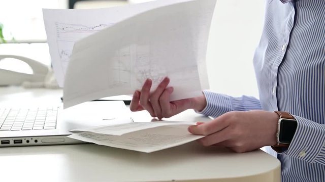 複数枚の書類を確認するデスクワークの女性。手元のみの撮影。