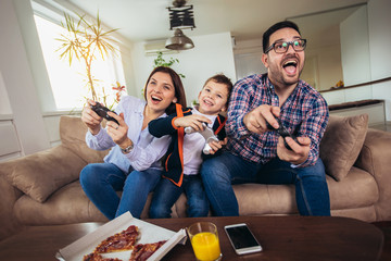 Happy family sitting on a sofa and playing video games and eating pizza © Mediteraneo