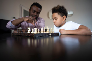 Cute african american son playing chess with his black father. The son teaches his father to play...