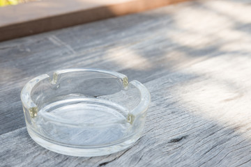 closeup glass ashtray transparent put on center of wooden table in the shadow of sun shine