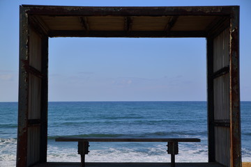 Bench inside wooden frame on seaside, view at blue ocean