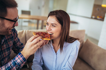 Beautiful young couple eating pizza,talking and smiling at home.