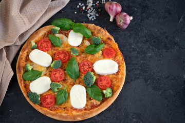 Italian pizza with Mozzarella cheese, tomatoes, broccoli, Spices and fresh basil. Pizza and kitchen napkin near, on black stone background