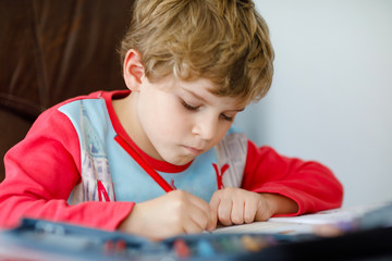 Portrait of cute happy school kid boy at home making homework. Little child writing with colorful pencils, indoors. Elementary school and education. Kid learning writing letters and numbers