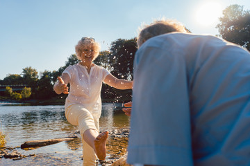 Full length of a funny senior couple playing with water at the river while enjoying their happy...