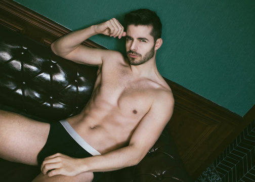 Attractive muscle guy posing with black briefs on leather sofa.