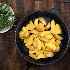 Potato wedges in iron cast skillet with rosemary herbs, olive oil and sea salt. Table top view