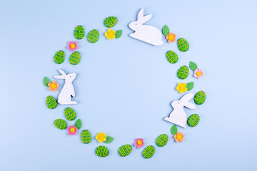 Easter holiday background. Top view of green sugar candy eggs, wooden bunny plased in a round frame on blue background. Flat lay, top view, copy space