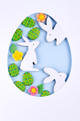 Easter egg frame made of paper, sugar candy eggs, bunny on blue background