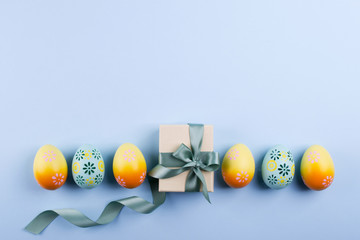 Easter holiday background with eggs. Top view of colorful painted chicken eggs plased  in a row and present box with ribbon