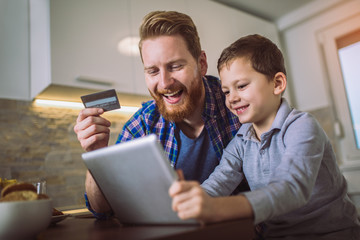 Father and son using digital tablet for online shopping at breakfast table