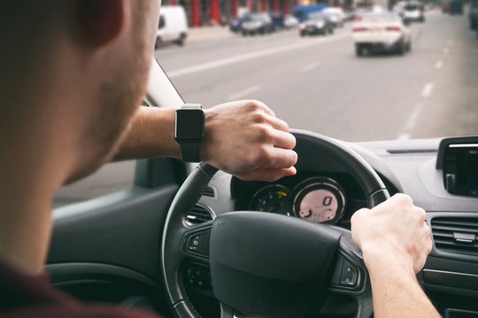 The young guy looking on his smartwatches on his hand sitting in the modern car