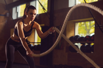 Fit, sporty and athletic sportswoman working in a gym. Woman training using battle ropes. Sports,...