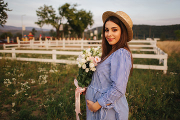 Obraz premium Back view of pregnant woman. She hold a bouquet of flowers and smile