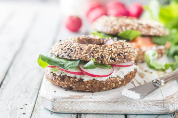 Bagels with cream cheese avocado, fish, arugula and radish on old wooden table. Healthy breakfast food.