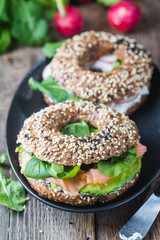 Bagels with cream cheese avocado, fish, arugula and radish on old wooden table. Healthy breakfast food.