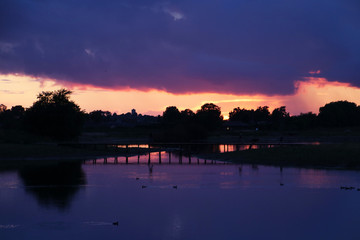 The birds gather in the lake where the water turned to purple by the dark clouds in the sunset.
