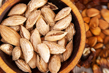 Unpeeled  almonds Badaam in a wooden cedar plate on the background a scattering of various nuts. Unpeeled  almonds Badaam pattern