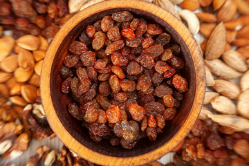 Brown raisins in a wooden cedar plate on the background a scattering of various nuts. Brown raisins pattern