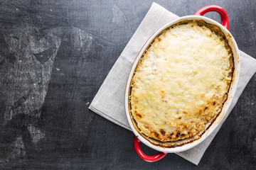 Casserole with chicken and zucchini on black background, top view