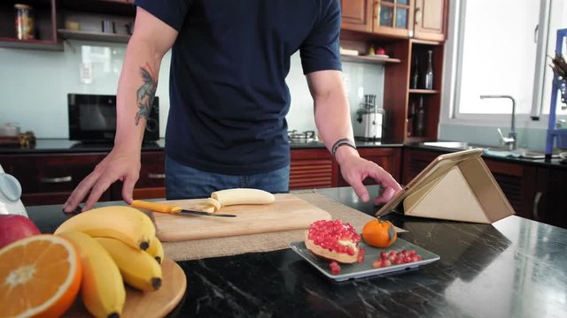 Lockdown of man turning on video recipe on tablet and starting cutting banana