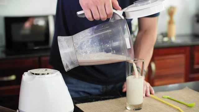 Close up of man pouring fresh milkshake from blender into glass, putting straw in it and starting drinking