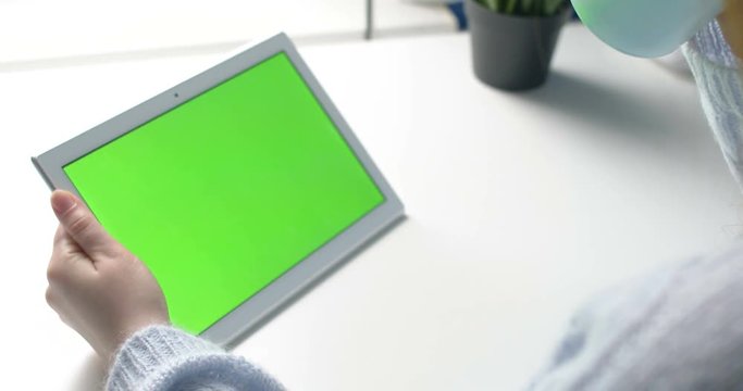 Young girl hold white taplet with green screen on table with coffe or tea cup. Close up 4k footage.