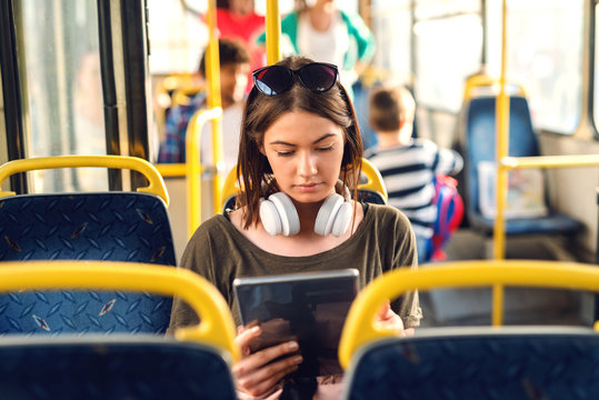 Pretty young girl with headphones sitting in a bus and watching tablet.